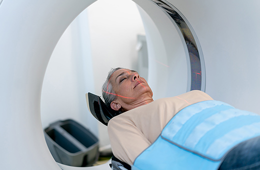 Mature woman lying down on a CT machine with eyes closed.