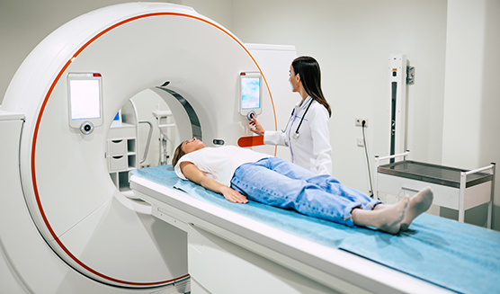 Female medical professional watching on as a woman laying on a table is put into a CT scan machine.