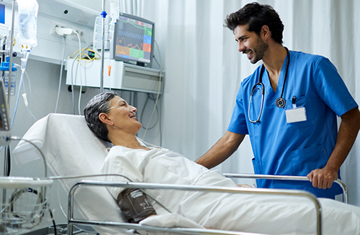 Male health care provider caring for man in hospital bed after surgery.