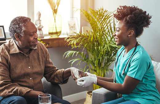 A doctor wearing gloves holds a patients hand while talking to him.