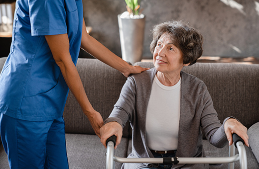 Woman sitting with her walker after hip replacement smiling at a health care provider.