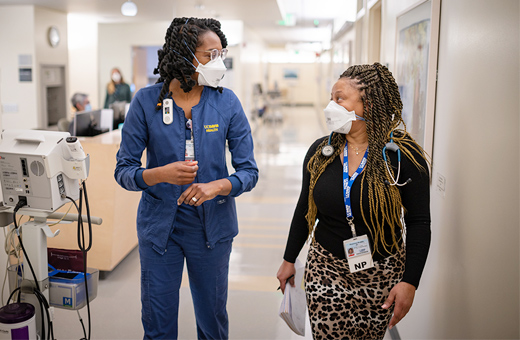 Two female healthcare providers walking down a hospital hallway