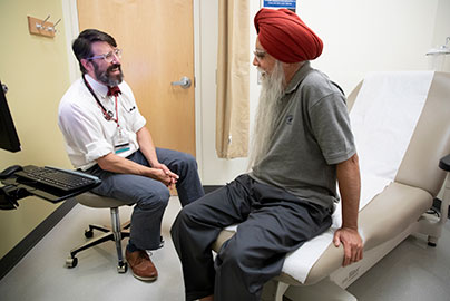Physician smiling while talking to an older man who is sitting on an exam table