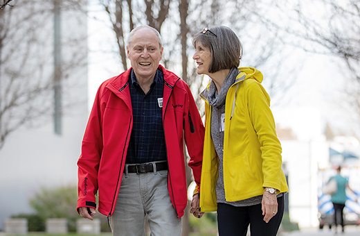 Older man and woman smiling and walking together holding hands outside.