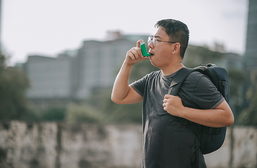 A man wearing a backpack using an inhalers outdoors.