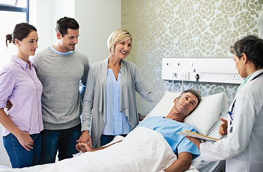 A male patient in a hospital bed surrounded by loved ones and a physician.