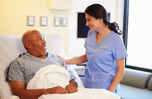 A male patient in bed and a nurse smile at each other. 