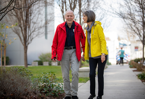 An older couple smile and walk along the sidewalk together.
