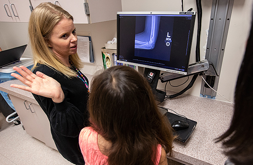 Female health care provider showing young patient x-ray image on an arm on a computer screen.