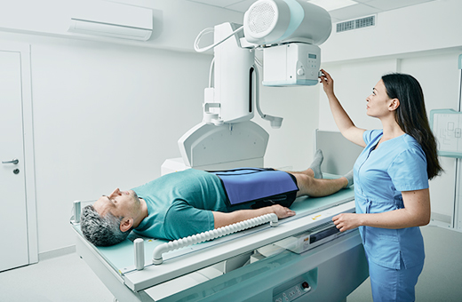 Female radiologist adjusting x-ray machine over man who is laying on a table r to get scanned.