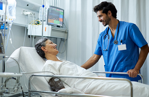 Patient in hospital bed smiling up at male health care provider watching over.