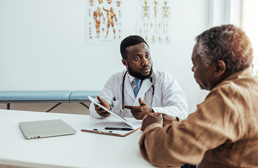 Male health care provider explaining information on a paper to a male patient at a desk.