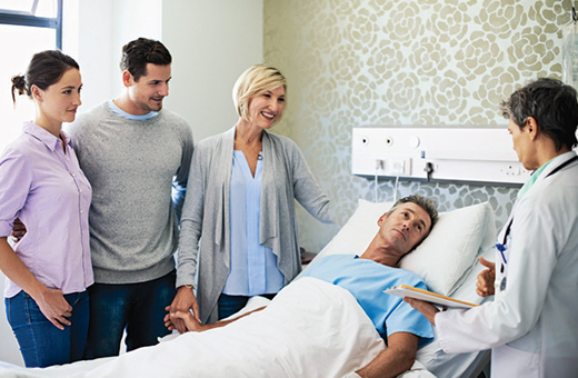 Male patient in hospital bed surrounded by loved ones and a health care provider