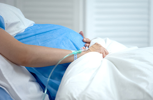 Pregnant woman laying in hospital bed with IV in her hand.