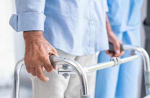Hands hold a walker while an occupational therapist stands nearby.
