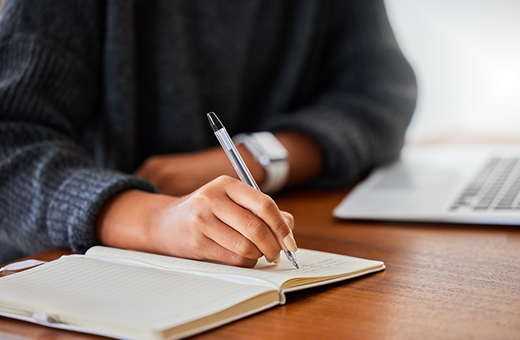 A woman holds a pen and writes on a pad of paper.