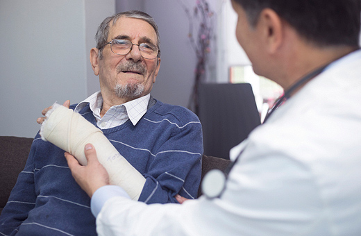 Male patient with a wrap on his wrist getting examined by orthopaedic surgeon after surgery in clinic.