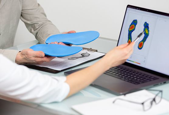 A patient holds molds of shoe inserts while a doctor points to a screen with a heat map of the patient’s feet.