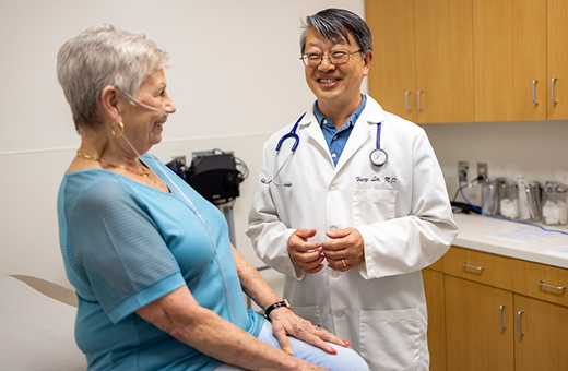 A patient and doctor talk and smile in an exam room.
