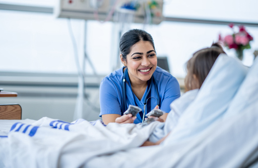 Health care provider smiling with child in hospital bed after heart surgery.