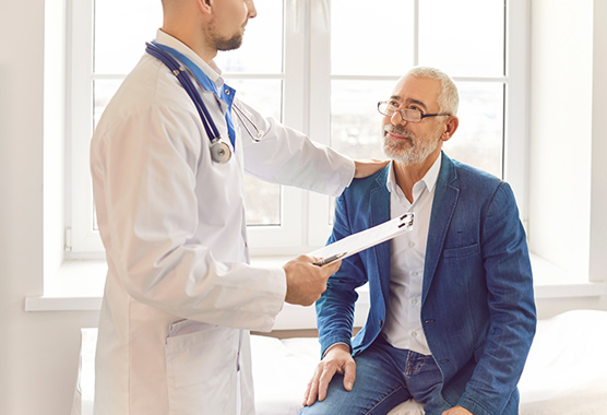A doctor places his hand on a sitting patient’s shoulder.
