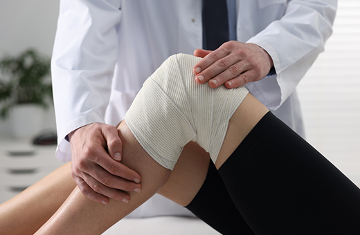A physical therapist supports a patient's bent knee that is wrapped in a bandage.