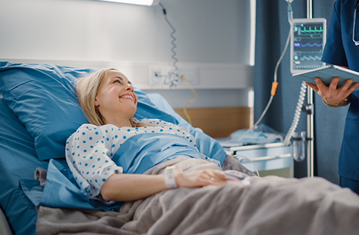 Woman in hospital bed after plastic surgery talking to health care provider.