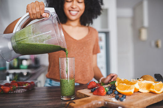 Woman pouring smoothie from a blender into a glass in the kitchen