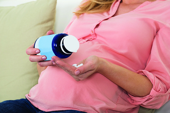 Midsection of pregnant woman pouring pills in hand from bottle 