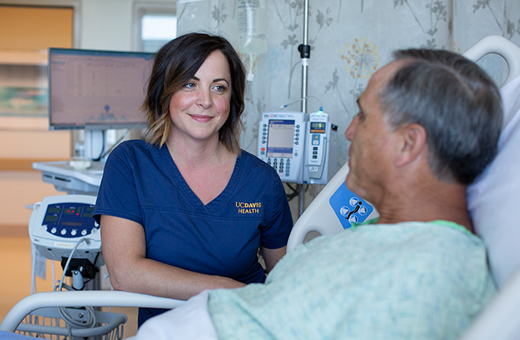 A nurse smiles at a male patient in a hospital bed.