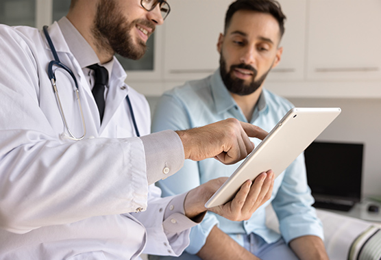 A doctor points to a tablet while speaking to a male patient.