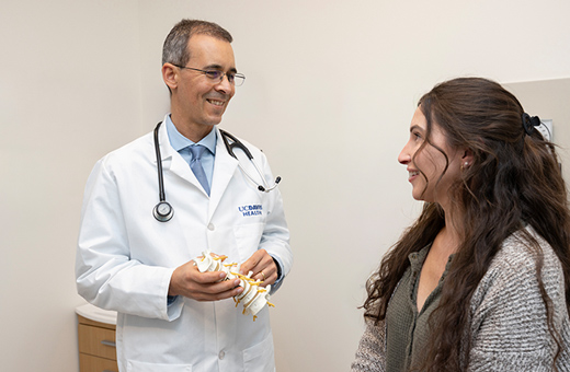 A doctor holds a model of a spine and speaks to a patient.