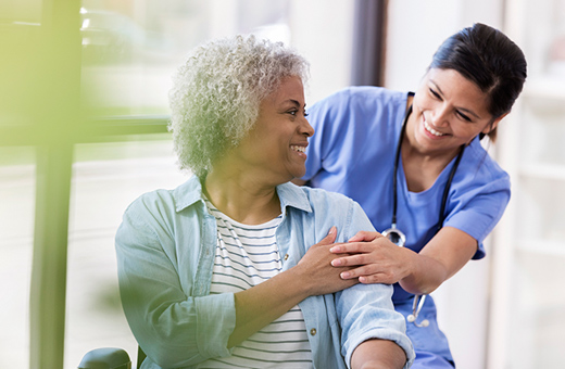 A nurse smiles and supports a woman in a wheelchair.