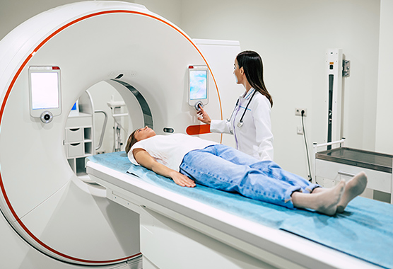 Female patient laying on a table going into a CT scan with health care provider standing next to her.