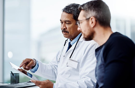 A doctor holding a clipboard discusses surgery with a patient.