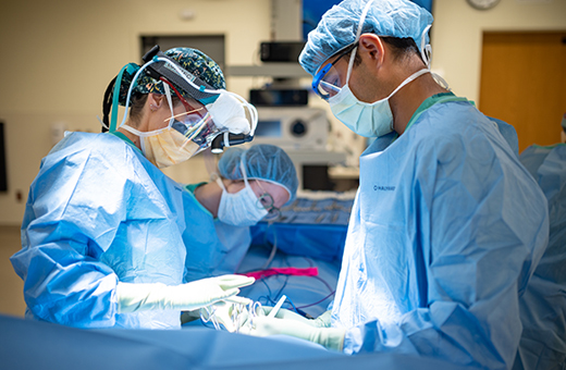 Surgeons in PPE work on a patient in the operating room.