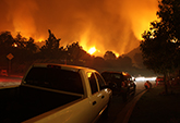 people outside their cars watching their neighborhood on fire