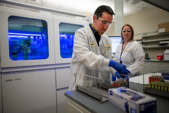 Lab scientists Marcelo Prado and Katie Zegarski prepare the cutting-edge lab robot to run hundreds of combined COVID-19/flu tests daily. 