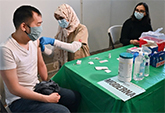 Justin Lau gets a bandage after his COVID-19 shot from UC Davis medical student Khadija Soufi as undergraduate Dana Hazem observes
