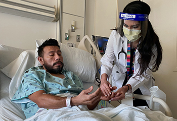 Residente en UC Davis Yesenia Ramos examina la pérdida de sensación de Saul Torres en los dedos, resultado de una complicación después del COVID