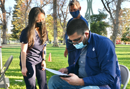 Oscar Pineda reviews his vaccination card with physician assistant student Thuy Nguyen and pediatrician Douglas Gross.