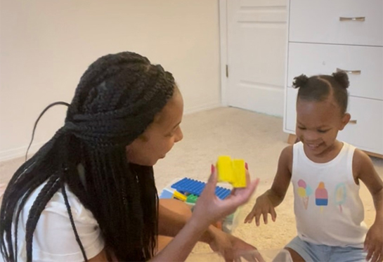 Black mother playing legos with her young child indoors.