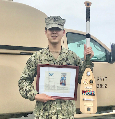 Navy Reservist Justin Choi holds paddle awarded to him at the conclusion of his service in the Navy Reserves