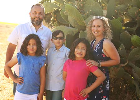 A family – mom, dad, two 10-year-old daughters and a 12-year-old son pose near a cactus. 