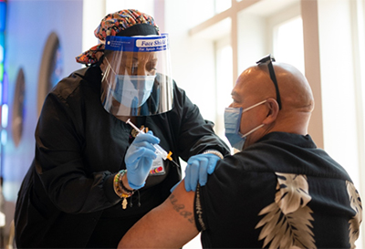 A nurse is administering COVID-19 vaccine to a middle-aged man