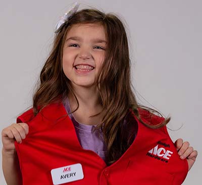 Pediatric patient poses with red Ace Hardware vest and nametag.