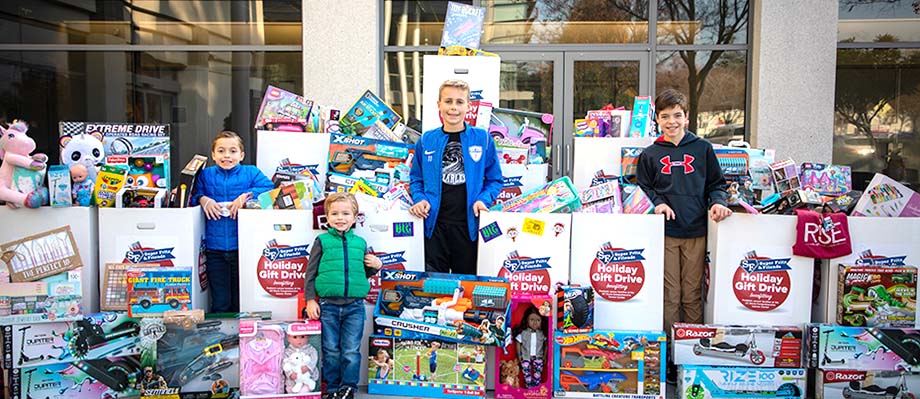 four boys standing next to toy drive bins