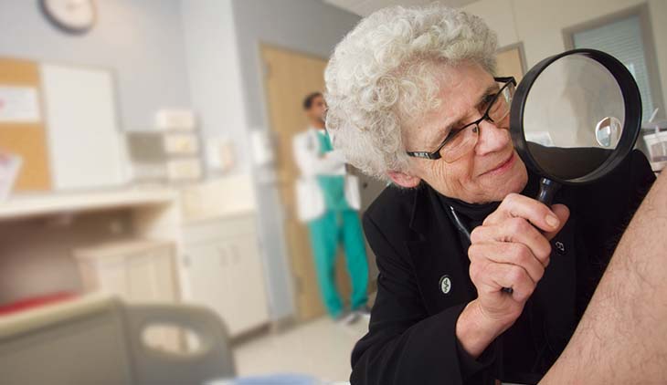 Dr. Faith Fitzgerald holding a magnifying glass looking at a patient&rsquo;s leg