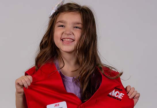 Pediatric patient poses with red Ace Hardware vest and nametag.