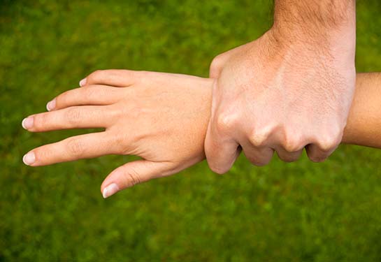 Man grabbing young woman's wrist with green grass background